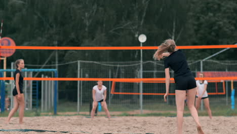 Young-woman-playing-volleyball-on-the-beach-in-a-team-carrying-out-an-attack-hitting-the-ball.-Girl-in-slow-motion-hits-the-ball-and-carry-out-an-attack-through-the-net.